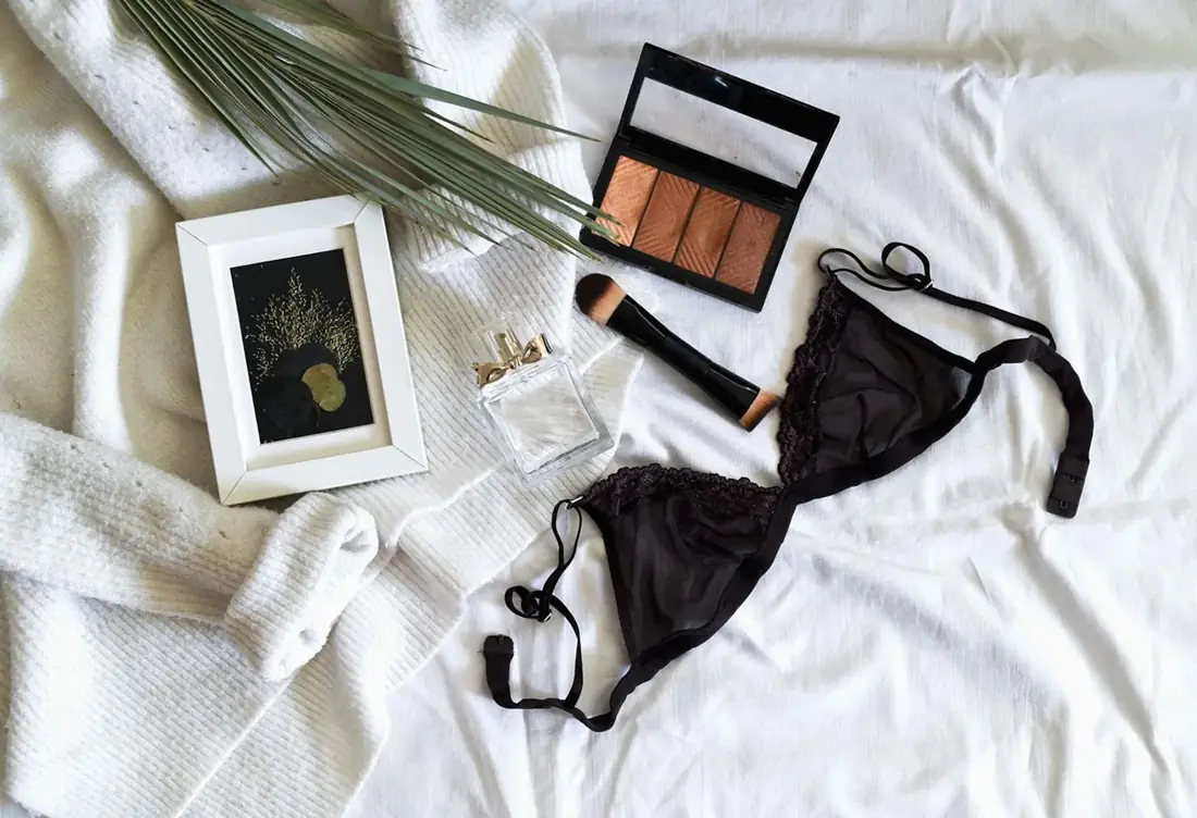Black lace bra laid on a white blanket beside a small picture frame
