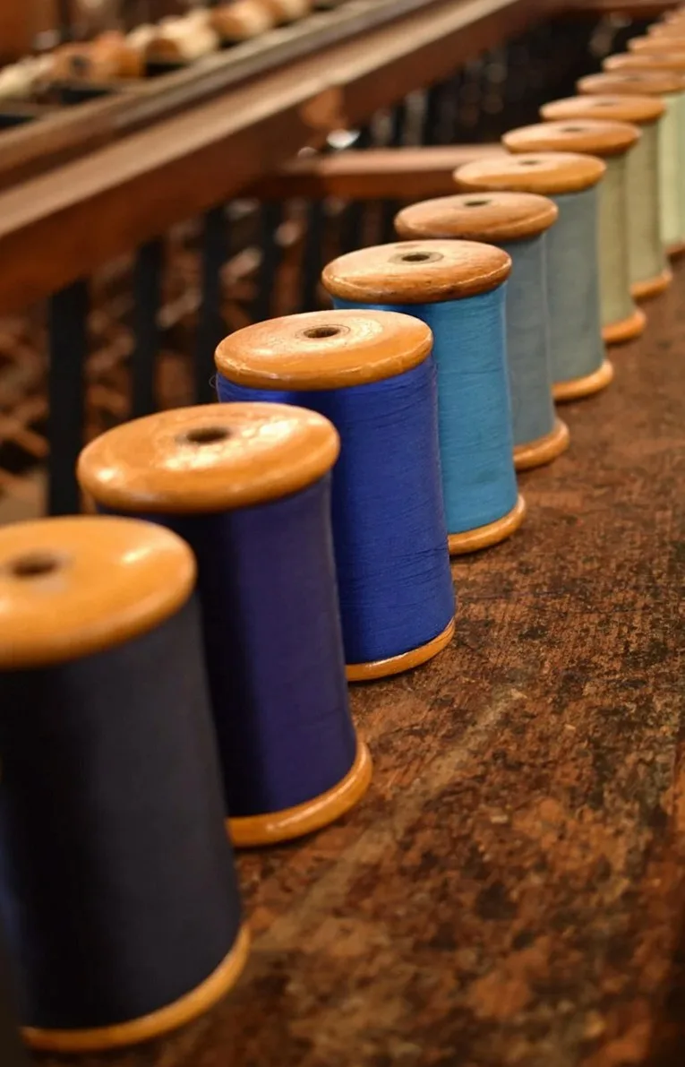 Row of blue and orange thread spools on a wooden rack